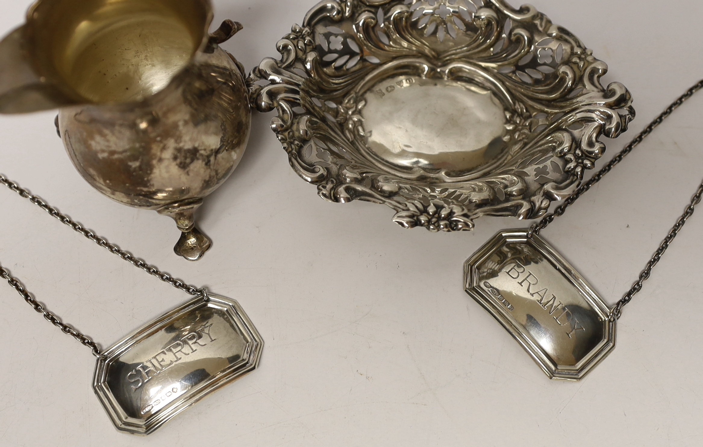 A late Victorian silver cream jug, Birmingham, 1894, 93mm, a repousse silver bonbon dish and a pair of modern silver wine labels.